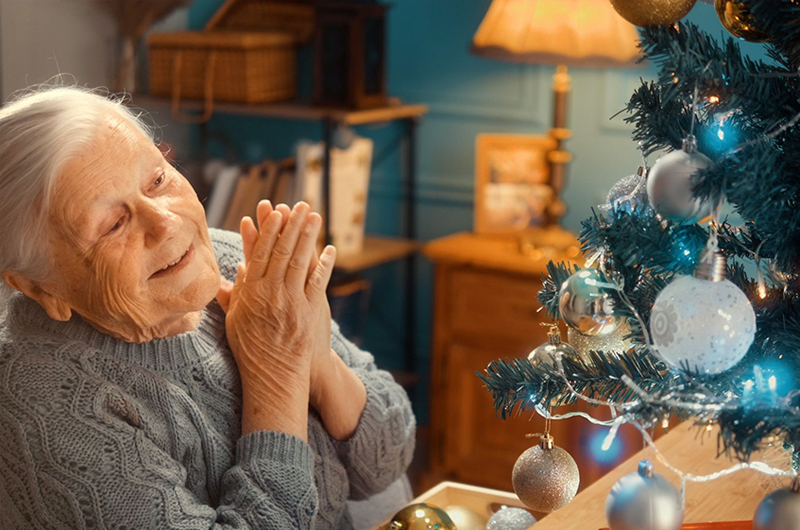 ältere Frau freut sich über ihren geschmückten Tannenbaum