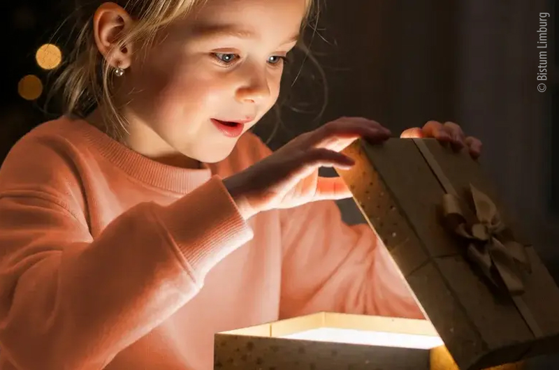 Mädchen öffnet mit leuchtenden Augen ein Geschenk